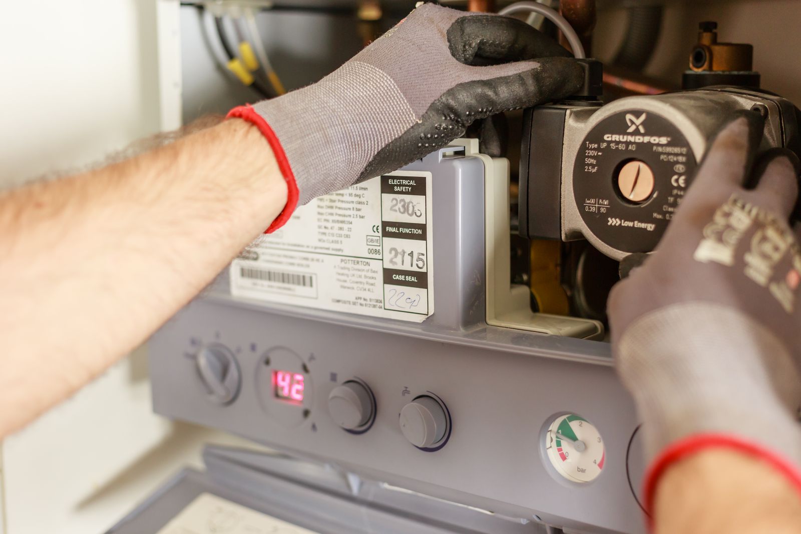 Gloved hands adjusting a boiler heating system with gauges