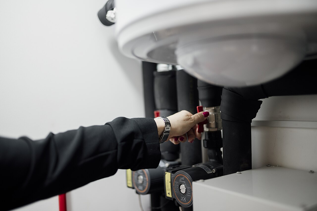 Hand turning a valve on plumbing under a sink, with pressure gauges