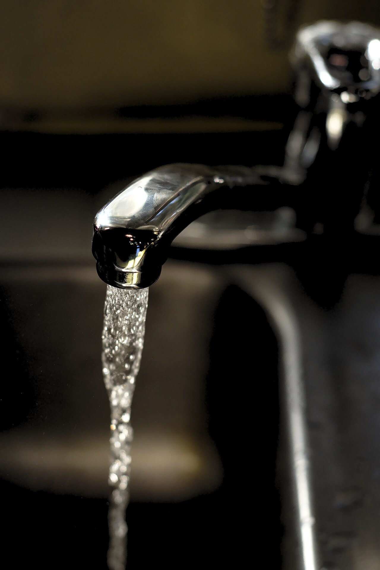 Chrome faucet with running water in a dark close-up